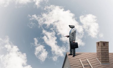 Evin çatısında baş durmak yerine kamerayla zum yapan yüzü olmayan bir iş adamı.