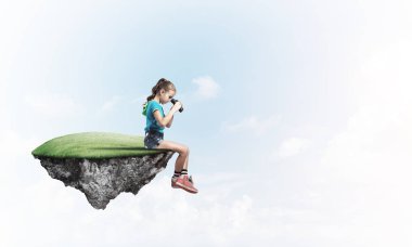 Gökyüzünde yüzen bir adada oturan tatlı, gülümseyen bir kız.