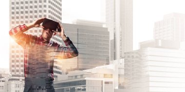 Sanal gerçeklik kulaklığı olan genç bir adam ya da şehrin arka planında 3 boyutlu gözlüklü.