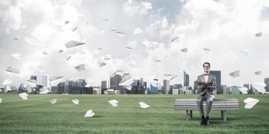 Kırmızı gözlüklü ve takım elbiseli komik adam bankta oturup kitap okuyor.