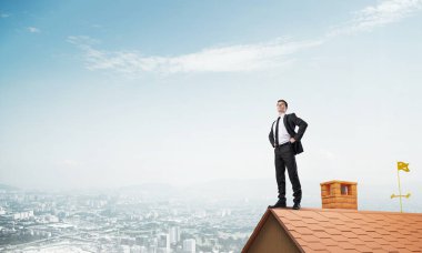 Kararlı genç işadamı evin çatısında dikiliyor ve başka tarafa bakıyor. Karışık ortam