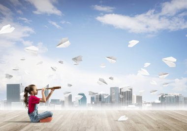 Ahşap zemin ve etrafında uçan kağıt uçaklar üzerinde oturan sevimli kız