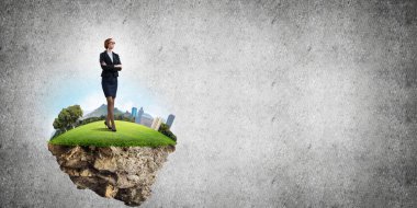 Yeşil yüzen adada beton zemine karşı duran kendine güvenen zarif bir iş kadını.