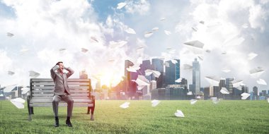 Hüsrana uğramış işadamı bankta oturuyor ve elleriyle kulaklarını kapatıyor.