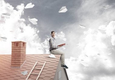 Elinde kırmızı kitap ile ev üzerinde oturan genç adam