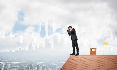 Genç işadamı dürbünüyle şehir manzarasını izliyor. Karışık ortam