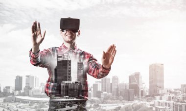 Sanal gerçeklik kulaklığı olan genç bir adam ya da şehrin arka planında 3 boyutlu gözlüklü.