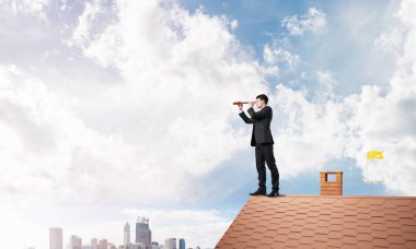 Genç kararlı işadamı çatının tepesinde dikilip dürbüne bakıyor. Karışık ortam