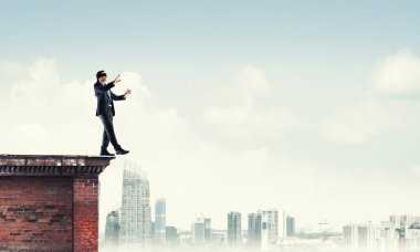 Binanın tepesinde gözü kapalı yürüyen bir iş adamı.