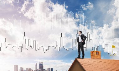 Kararlı genç işadamı evin çatısında dikiliyor ve başka tarafa bakıyor. Karışık ortam