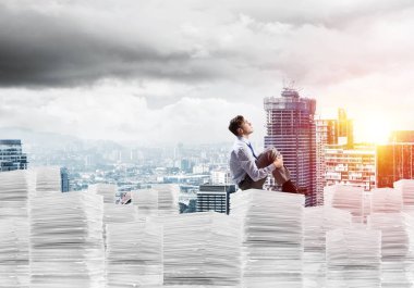 Düşünceli işadamı uzak belgeler cityscape ve arka plan üzerinde güneş ışığı ile yığını üzerinde otururken arıyorum. Karışık teknik.