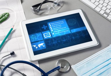 Gri yüzeyde beyaz tablet ve doktor araçları