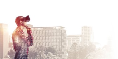 Sanal gerçeklik kulaklığı olan genç bir adam ya da şehrin arka planında 3 boyutlu gözlüklü.