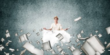 Adam beyaz giyim gözler tutmak kapalı ve seyir üzerinde uçan bulut kitaplar ile gri karanlık duvar arka plan üzerinde uçan arasında meditasyon sırasında konsantre.