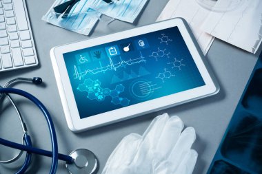 Gri yüzeyde beyaz tablet ve doktor araçları