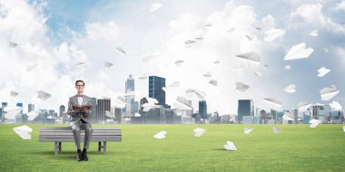 Kırmızı gözlüklü ve takım elbiseli komik adam bankta oturup kitap okuyor.