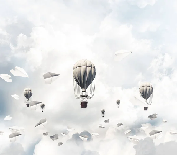 Colorful aerostats flying among paper planes and over the blue cloudy sky. 3D rendering.