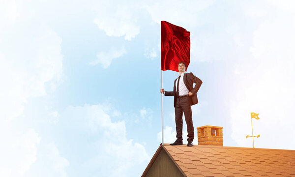 Businessman standing on house roof and holding red flag. Mixed media