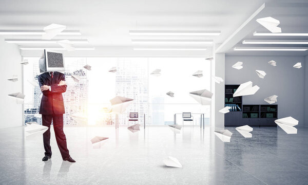 Бизнесмен в костюме с монитором вместо головы держит руки скрещенными, стоя среди летающих бумажных самолетов внутри офисного здания. 3D рендеринг
.