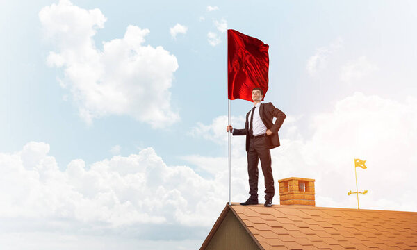 Businessman standing on house roof and holding red flag. Mixed media