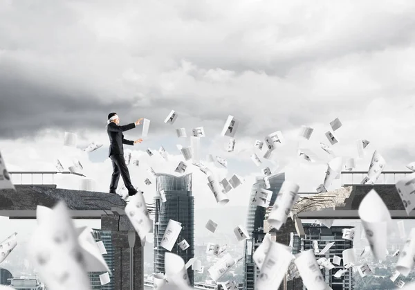 Kağıtları kocaman bir boşluk ile beton köprü üzerinde gizli tehditler ve riskler sembolü olarak uçan arasında blindfolded yürüyüş iş adamı. Cityscape görünümü arka plan üzerinde. 3D render.