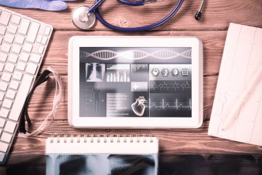 Beyaz tablet bilgisayar ve doktor aletleri ahşap masada.