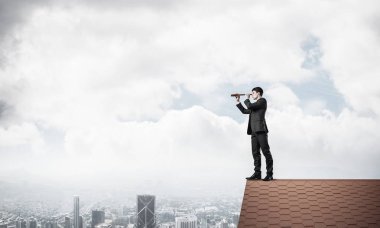 Genç kararlı işadamı çatının tepesinde dikilip dürbüne bakıyor. Karışık ortam