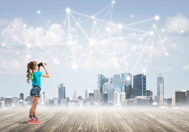 Şirin kız ahşap bir zeminde duruyor ve dürbünle izliyor.