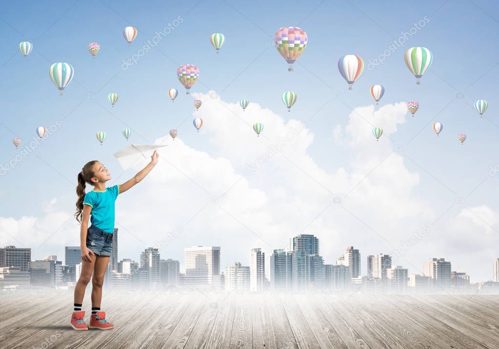 Cute kid girl standing on wooden floor and aerostats flying in air