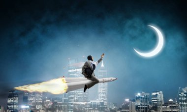 Arka plan üzerinde moon ile gece cityscape ve mavi karanlık gökyüzü ile roket üzerinde uçan takım elbiseli genç işadamı kavramsal görüntü.