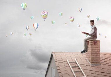 Elinde kırmızı kitap ile evin baca rahat oturan genç adam