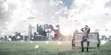 Hüsrana uğramış işadamı bankta oturuyor ve elleriyle kulaklarını kapatıyor.