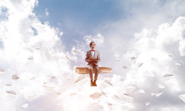 Komik adam kırmızı gözlük ve etrafında uçan kitap ve kağıt uçaklar üzerinde oturan takım elbise