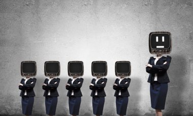Eski televizyonlu takım elbiseli iş kadınları kollarını kavuşturup arka planda gri duvarla boş bir odada duruyorlar..