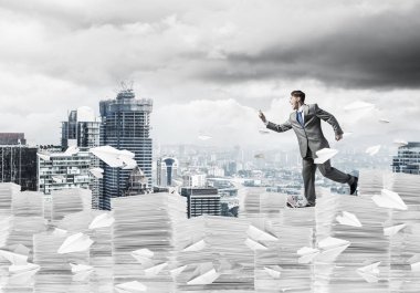 Siyah takım elbise ile telefonu elinde kağıt uçaklar ile cityscape arka plan üzerinde uçan arasında çalışan işadamı. Karışık teknik.