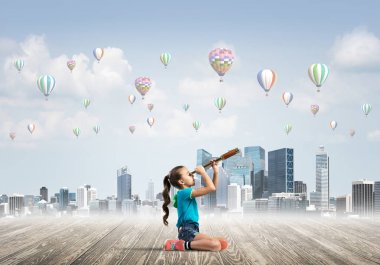 Ahşap zeminde oturan tatlı kız ve havada uçuşan hava yastıkları.