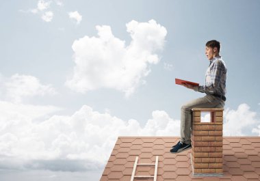 Elinde kırmızı kitap ile evin baca rahat oturan genç adam