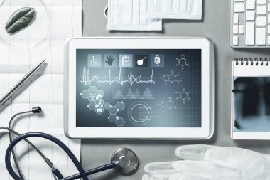 Gri yüzeyde beyaz tablet ve doktor araçları