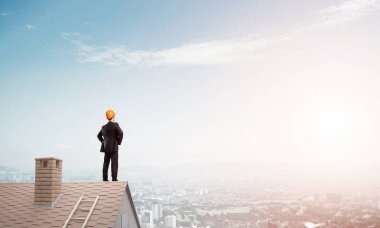 Takım elbiseli genç işadamı ve çatıda kask var. Karışık ortam