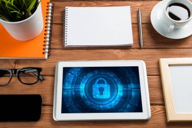 Ofis eşyalarıyla iş yeri ve ekranda asma kilit simgeleri olan tablet