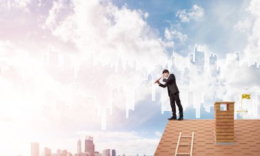 Çatıda takım elbiseli genç bir işadamı var. Karışık ortam