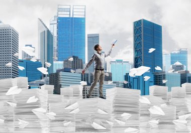 Sıradan giyinen adam kitapla el ele tutuşurken arka planda şehir manzarası olan uçan kağıt uçakların arasında dikiliyor. Karışık ortam.