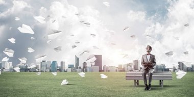 Kırmızı gözlüklü ve takım elbiseli komik adam bankta oturup kitap okuyor.