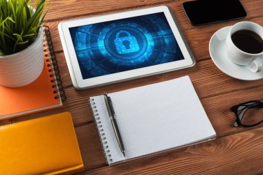 Ofis eşyalarıyla iş yeri ve ekranda asma kilit simgeleri olan tablet