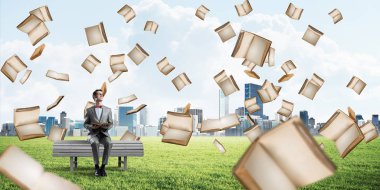 Kırmızı gözlüklü ve takım elbiseli komik adam bankta oturup kitap okuyor.