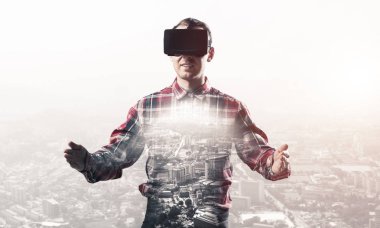 Sanal gerçeklik kulaklığı olan genç bir adam ya da şehrin arka planında 3 boyutlu gözlüklü.