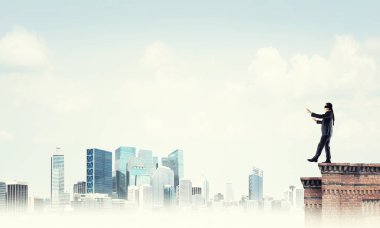 Binanın tepesinde gözü kapalı yürüyen bir iş adamı.