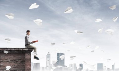 Elinde kırmızı kitap ile üst yapı üzerinde rahat oturan genç adam