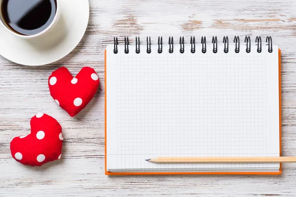 Coffee cup notepad pencil and two red hearts on wooden surface