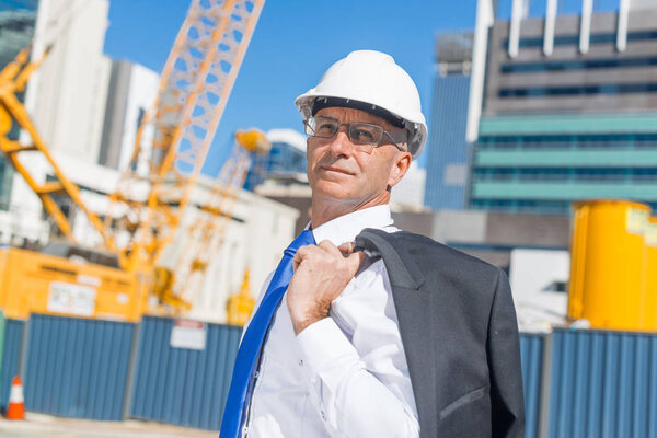 Confident construction engineer in hardhat and with jacket on shoulder